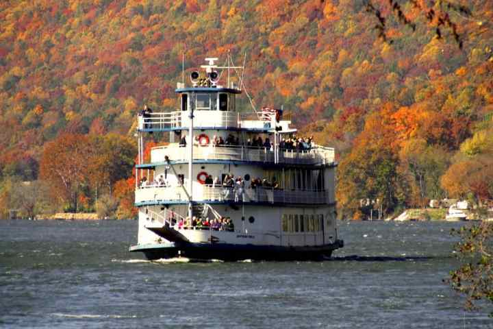 Riverboat on water with colorful autumn trees on hillside in the background.