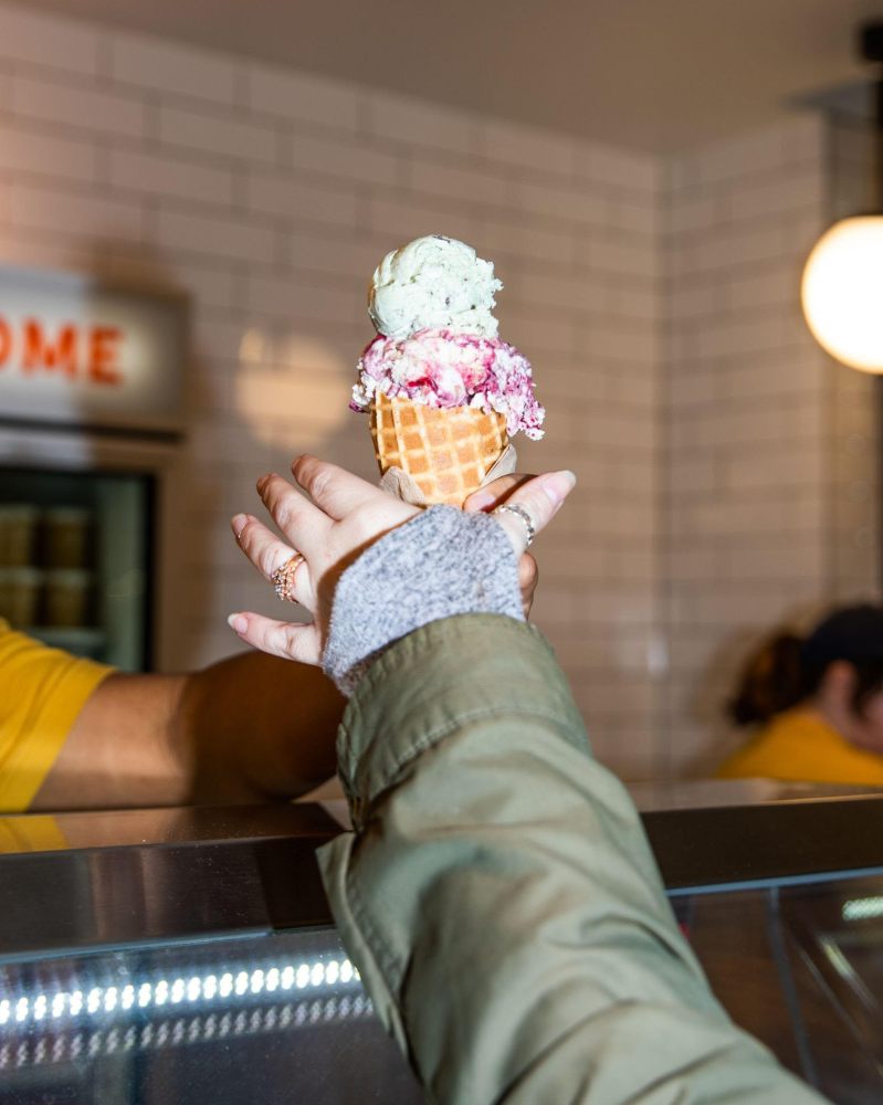 Person handing a triple scoop ice cream cone over a counter.